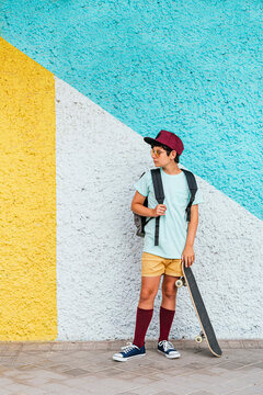 Boy with cap and skateboard standing on footpath