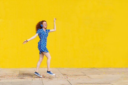 Carefree woman listening music while dancing by yellow wall