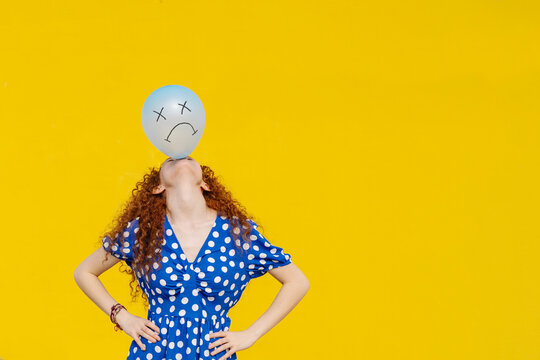 Young woman with hand on hip balancing balloon in front of yellow wall