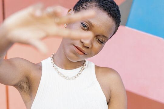 Woman winking while gesturing peace sign in front of multi colored wall