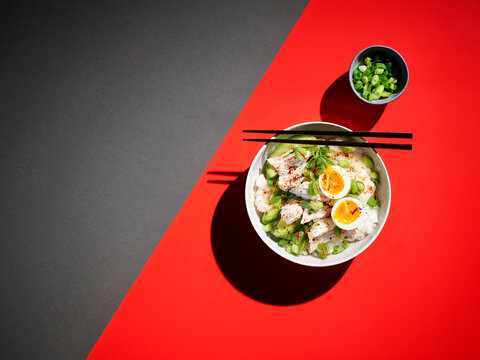 Studio shot of bowl of congee with chicken breasts, boiled egg, avocado and scallions