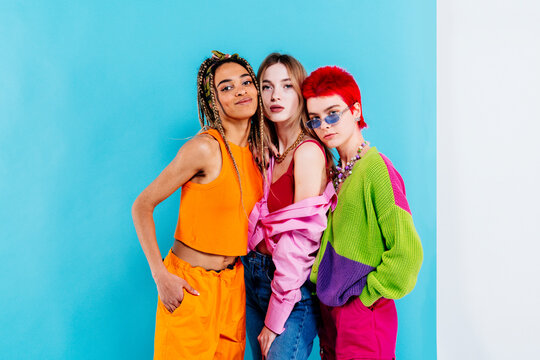 Stylish female friends standing against blue background
