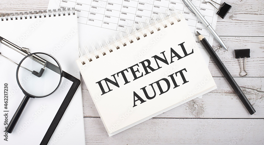 Poster notepad with text internal audit with a pen,office tools and graphs on desktop.