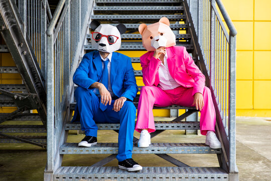 Man and woman wearing vibrant suits and bear masks sitting together on metal stairs