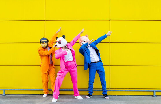 Three adults wearing vibrant suits and animal masks dabbing together in front of yellow wall