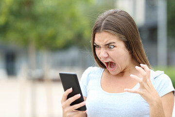 Angry teen watching media on smartphone - obrazy, fototapety, plakaty