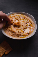Chickpeas hummus with olive oil and toasted sesame on dark background and selective focus. 