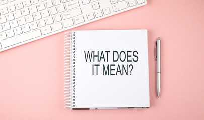 Pink office desk with keyboard and notebook with text WHAT DOES IT MEAN