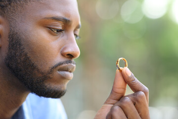 Sad black husband doubting holding wedding ring - obrazy, fototapety, plakaty