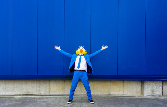 Man wearing vibrant blue suit and bird mask standing outdoors with raised arms