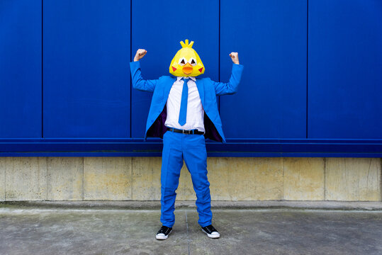 Man wearing vibrant blue suit and bird mask flexing muscles in front of blue wall