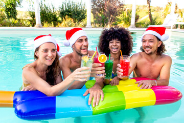 merry christmas! happy diverse group of friends wearing xmas santa hat having drinks making a toast with cocktails on swimming pool party celebrating winter warm festivities outdoors. summer holidays