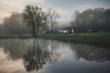 Early foggy morning at the pond. Reflection of trees in the water. Spring morning.