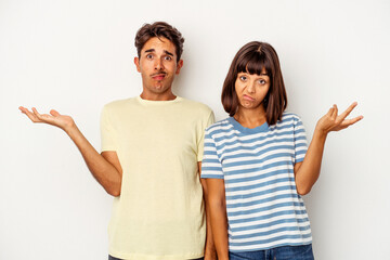 Young mixed race couple isolated on white background doubting and shrugging shoulders in...