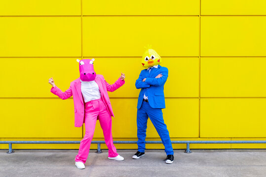 Man and woman wearing vibrant suits and animal masks posing together in front of yellow wall