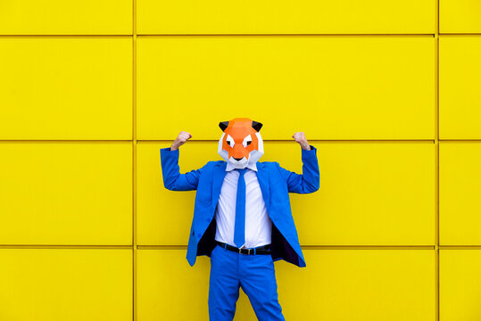 Man wearing vibrant blue suit and tiger mask flexing in front of yellow wall