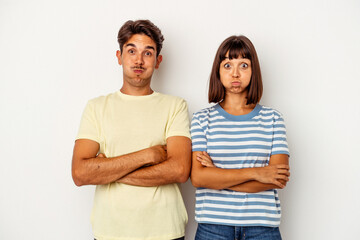Young mixed race couple isolated on white background blows cheeks, has tired expression. Facial expression concept.