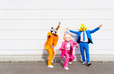 Three people wearing vibrant suits and animal masks posing side by side in front of white wall