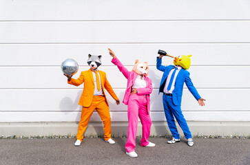 Three people wearing vibrant suits and animal masks partying in front of white wall