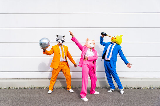 Three people wearing vibrant suits and animal masks partying in front of white wall