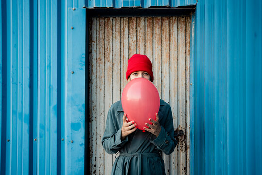 Woman holding balloon in front of corrugated metal door