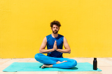 Mid adult man sitting with hands clasped while practicing Padmasana in front of yellow wall