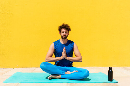 Mid adult man sitting with hands clasped while practicing Padmasana in front of yellow wall