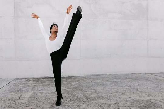 Flexible male dancer looking up while stretching leg against wall