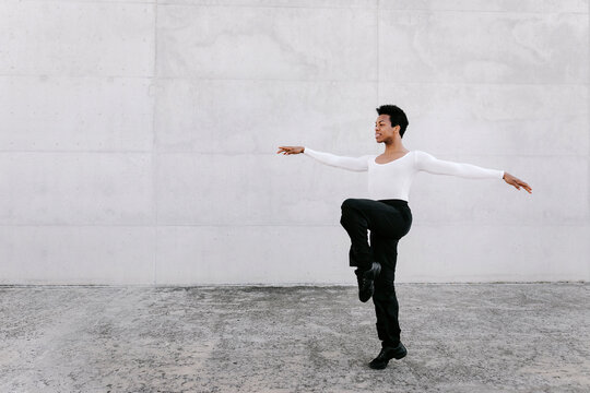 Urban dancer balancing on tiptoe while dancing against white wall