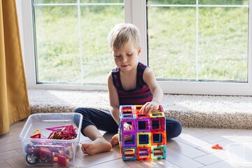 The child is playing with a multi-colored magnetic constructor, building a tower. Educational toys...