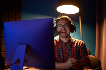 Happy young guy creating podcast sitting at table with computer and microphone