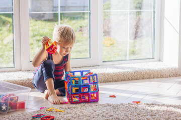 The child is playing with a multi-colored magnetic constructor, building a tower. Educational toys...