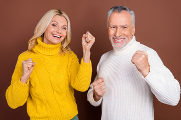 Portrait of two attractive cheerful grey-haired people celebrating having fun isolated over brown color background