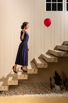 Woman looking at red helium balloon while moving up on staircase