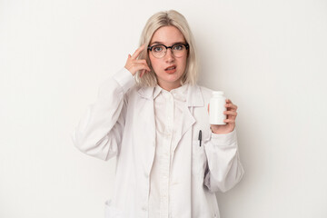 Young pharmacist woman holding pills isolated on white background showing a disappointment gesture with forefinger.