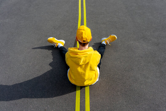 Boy sitting over yellow road marking on sunny day