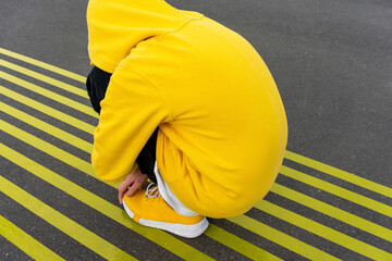 Lonely boy hugging knees while crouching on yellow road markings