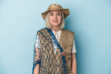 Young caucasian fisherwoman holding a net isolated on blue background happy, smiling and cheerful.