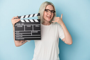 Young caucasian woman holding a clapperboard isolated on blue background showing a mobile phone...