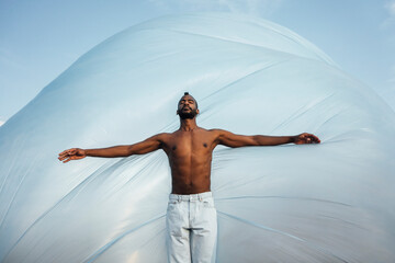 Shirtless man with arms outstretched standing in front of foil