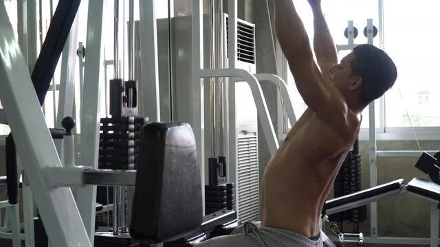 fit man shirtless exercises with  rowing machine in fitness club  . Muscular man workout  pumping up muscles chest with cable crossover at gym . bodybuilder training in sport center