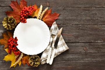 Autumn Thanksgiving table setting for with plate, knife, fork decorated pumpkins, napkin, fir cones, rowan berry and maple leaves on a wooden table. Concept of Thanksgiving day or Halloween. Top view