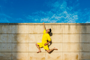 Man hanging on wall with one hand during sunny day