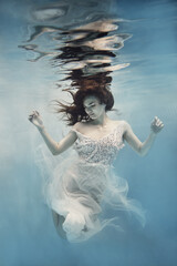 A girl with dark hair in a white dress swims underwater as if flying in zero gravity