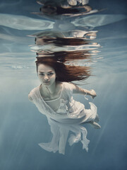 A girl with dark hair in a white dress swims underwater as if flying in zero gravity