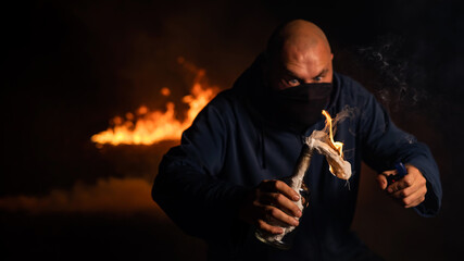 A masked man is holding a burning bottle. Molotov cocktail.