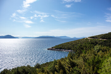 Fototapeta na wymiar Green cliffs sunny sea shore on a bright clear blue day in Greece. Sun beam on water and blue sky, Lefkada island, Ionian sea coast