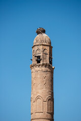 Ancient sandstone minaret with loudspeakers and storks nest on top
