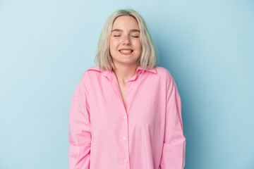 Young caucasian woman isolated on blue background laughs and closes eyes, feels relaxed and happy.