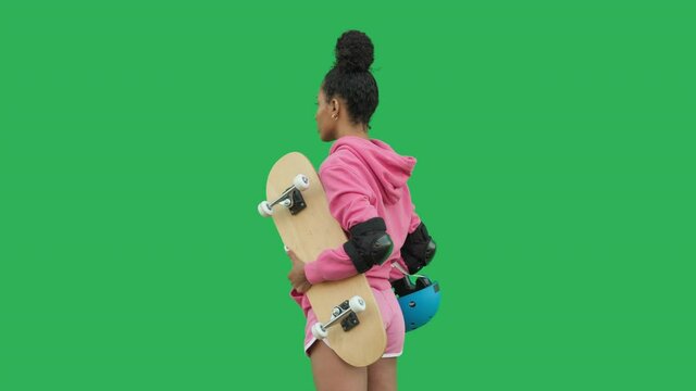 Portrait of young african woman with skateboard rotating in front of camera over green background. Sporty girl holding board. Concept of lifestyle, multiethnic, recreation, sports. Chroma key